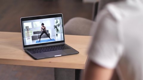 Close-up of laptop screen with live stream of joyful mixed race woman trainer practicing yoga warrior pose during online workout with male, remote home training, e-learning, healthy sport lifestyle