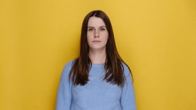 Happy overjoyed young woman doing winner gesture clenching fists dancing say yes, looking at camera, dressed in blue sweater, isolated on yellow background studio. Emotion people lifestyle concept