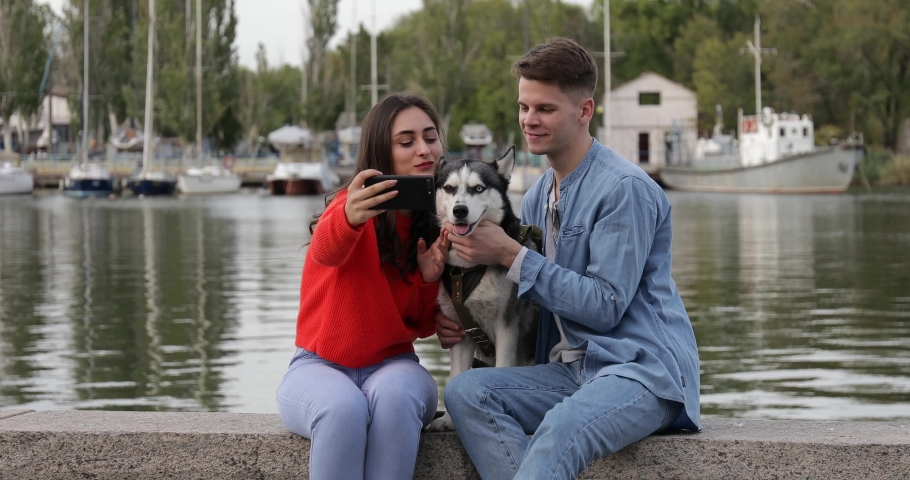 Young couple with cute husky dog taking selfie near river