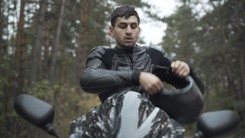 Portrait of handsome Middle Eastern man putting on motorcycle helmet and leather biker gloves. Confident serious male motorcyclist sitting on motorbike. Racing and lifestyle concept. | Shutterstock HD Video #1063425076