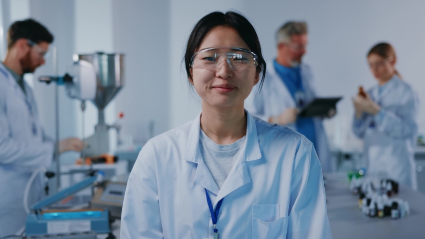 Asian portrait woman scientist with protective glasses look at camera smiling feel happy. Background team work. Microbiology pharmaceutical biochemistry medical technology. Slow motion Royalty-Free Stock Footage #1063426288