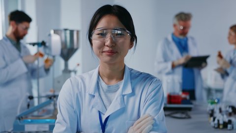 Asian portrait woman scientist with protective glasses look at camera smiling feel happy. Background team work. Microbiology pharmaceutical biochemistry medical technology. Slow motion
