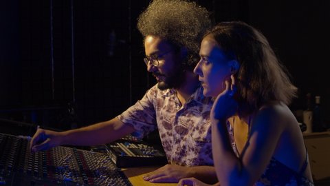 Music recording studio. Creative people. Hispanic man and woman working in the sound studio. Brunette curly latin couple is producing songs and having a good time. 