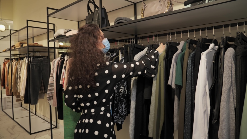 Shopping Quarantine, a pretty female customer wearing medical masks chooses clothes after the quarantine is removed during a pandemic in a fashion boutique in a mall Royalty-Free Stock Footage #1063431142
