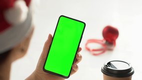 Close-up shot of green screen template smartphone in female hands at home offise. The template can be used to advertise purchases on Christmas Eve. Modent technology and information concept. POV
