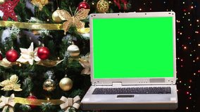 Vintage laptop with green screen and Christmas tree with blinking lights behind