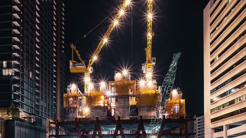Time-lapse of crane and construction worker in under construction building site at night. Construction industry, industrial business, or civil engineering technology concept. Zoom out