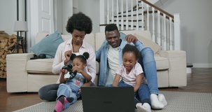 Adorable satisfied happy loving african american couple with their two small daughters sitting on the floor and playing videogame on computer,family leisure concept,4k