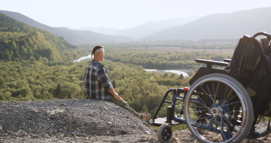 Side view of good-natured happy joyful handicapped guy which sitting on the hill