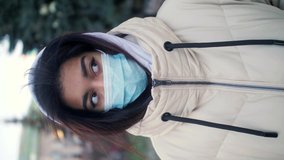 Vertical format portrait footage of young teenage girl in medical face mask posing for camera outdoor. Environment. Beautiful diverse multiethnic hispanic female.
