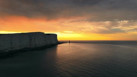 Landscape aerial drone footage video of a Beachy Head Lighthouse and chalk cliffs at colourful sunrise  with low tide in England, near Eastbourne