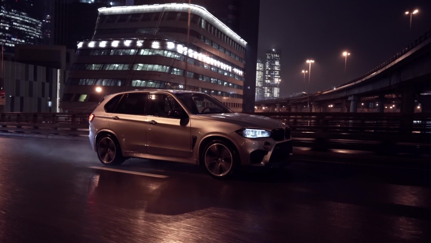 Moscow, RUSSIA - NOVEMBER 29, 2020: crane moving rolling shot of a grey BMW X5M powerful SUV driving on a city at rainy night. Concept of business, traveling, luxury, lifestyle