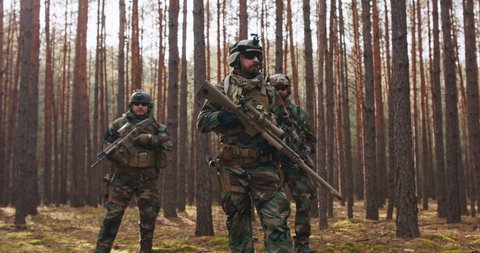 Four Fully Equipped Middle - Aged Soldiers Wearing Camouflage Uniform Attacking Enemy, They're in Shooting Ready Stance, Aiming Rifles. Military Operation in Action, Squad Standing in Dense Forest.