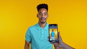 Smiling vlogger african man recording video of hisself dancing in front of smartphone camera on yellow background. Influencer makes funny social media clip