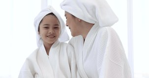 Mother and daughter in white bathrobes are having fun spa treatments.