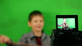 Blogging topic. A child in front of the camera records video on a green background. The boy writes a blog on the camera. Online lesson. The child is out of focus. Selective focus. Green screen