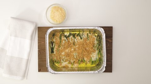 Asparagus casserole in a creamy Alfredo sauce topped with bread crumbs and Parmesan cheese. Chef topping asparagus with Parmesan cheese, close up video, view from above