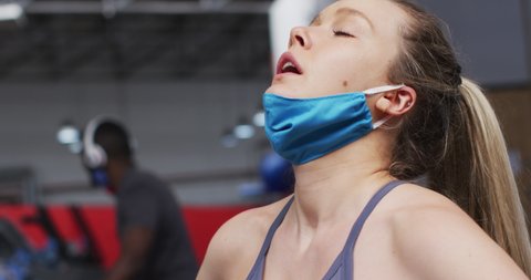 Caucasian woman wearing lowered face mask exercising at gym. wiping sweat from brow with hand during workout. exercising at the gym during coronavirus covid 19 pandemic.