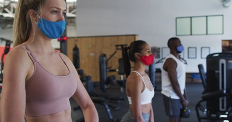 Two fit caucasian women and fit african american man wearing face masks exercising using kettlebell in the gym. social distancing quarantine lockdown during coronavirus pandemic