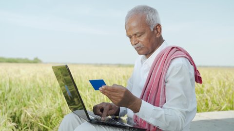 Indian farmer on laptop doing payment by using credit card - concept of rural people using technology, internet and lifestyle