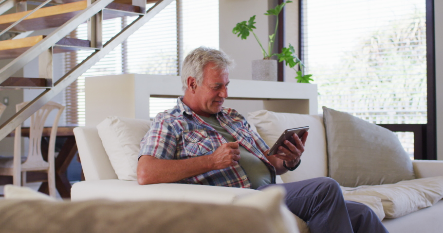 Senior caucasian man having a video chat on digital tablet while sitting on couch at home. social distancing quarantine lockdown during coronavirus pandemic | Shutterstock HD Video #1063460347