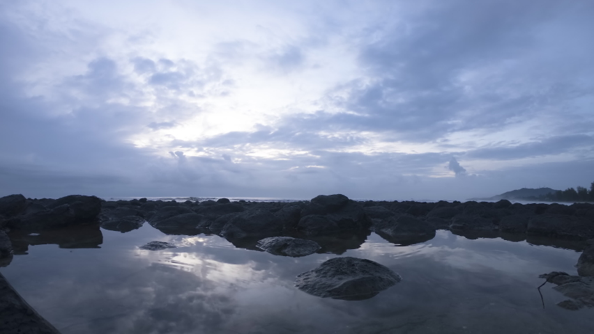 4K time lapse scene at the beach with basalt rocks and reflection during cloudy sunrise.