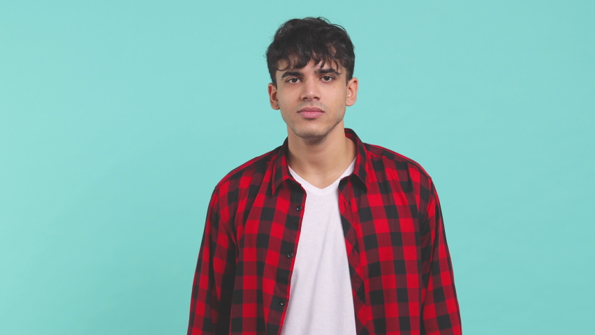 Cheerful funny smiling young man 20s wearing basic red checkered shirt posing isolated on blue turquoise color background in studio. People lifestyle concept. Dancing clenching fists waving hands Royalty-Free Stock Footage #1063462018