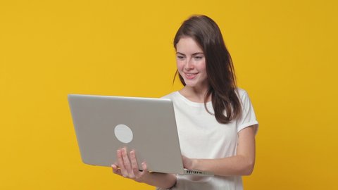 Excited funny brunette young woman 20s years old wearing casual white t-shirt posing isolated on yellow color background studio. People lifestyle concept. Pointing index finger on laptop pc computer