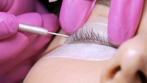 Face of a young girl before a modern eyelash lamination procedure in a professional beauty salon. The master applies special glue before the eyelash curling procedure in pink rubber gloves close up.