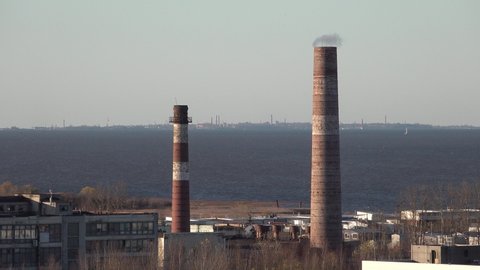 Factory with red pipes on the sea shore of the lake bay. There is smoke or steam. Kronstadt island on background