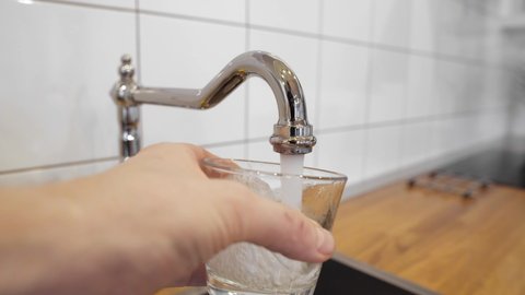 male's hand pouring water into the glass from chrome faucet to drink running water with air bubbles. potable water and safe to drink. man filling a glass of water from a stainless steel kitchen tap.