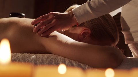 Young and beautiful woman gets hot stone massage therapy in the spa salon. Healthy lifestyle and body care concept.