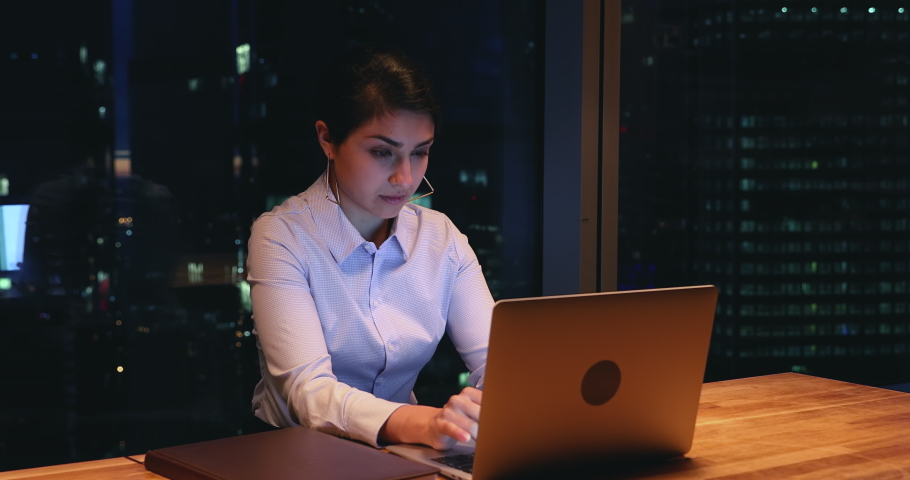 Tired overworked workaholic indian female employee sit at workplace desk in modern office using laptop working on deadline task, urgent project feels exhausted. Over hours job, hard-working concept | Shutterstock HD Video #1063468537
