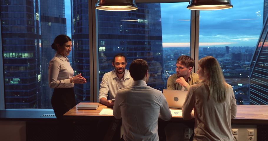 Multiethnic startup business team gathered in modern office boardroom, working until late, skyscrapers, night city view through panoramic window. Motivated ambitious workgroup brainstorming concept | Shutterstock HD Video #1063468561
