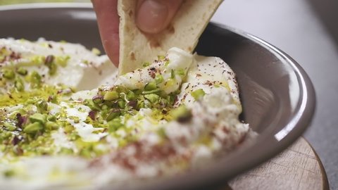 Dipping a piece of bread in homemade labneh with pistachios.