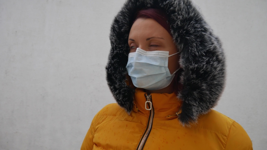 Woman in a yellow jacket with a fur hood and a medical mask over her face at dark. 