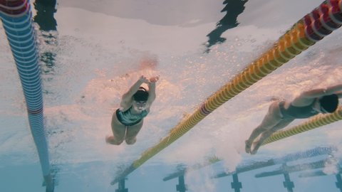 Underwater video of young students in athlete swimming suits and swimming goggles training butterfy stroke in the indoor swimming pool. Front view.