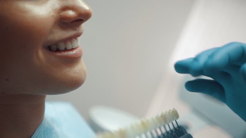 A male dentist uses a teeth whitening table to select a color for a smiling patient. Dental treatment and care. Oral hygiene. Health care and medicine concept.