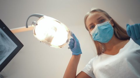 Young beautiful caucasian doctor dentist moves the lamp to examine the patient's oral cavity.