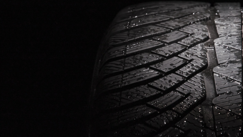 Slow Rotation of a Car Tire. The geometric pattern of the wheel in water droplets slowly rotates towards the viewer. Drops sparkle on the black rubber on a black background | Shutterstock HD Video #1063490770