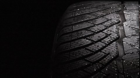 Slow Rotation of a Car Tire. The geometric pattern of the wheel in water droplets slowly rotates towards the viewer. Drops sparkle on the black rubber on a black background
