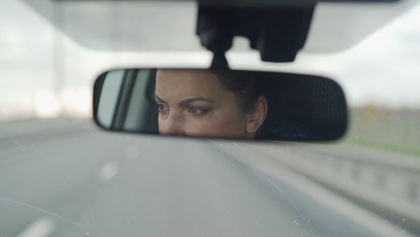 Brunette woman sitting behind the wheel driving car female driver face in rear view mirror closeup. | Shutterstock HD Video #1063493794