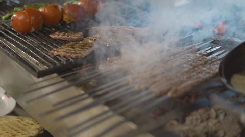Traditional Turkish cuisine cooked in Adana Kebab grill. Chef cooking meat on barbecue grill for customers. Traditional Turkish shish kebab and vegetables on barbecue fire.