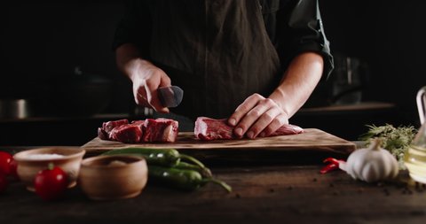 Chef cutting meat with a knife on kitchen table. Cooker is making a meal out of beef and vegetables on professional kitchen 4k footage