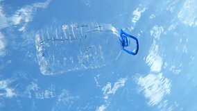 VERTICAL VIDEO: Big plastic bottle floats on the water surface, on background of the blue sky with clouds. Barrel with handle drifts on the sea waves. Plastic pollution of the Ocean. Underwater shot