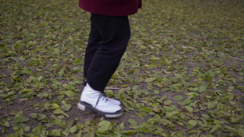 Attractive woman walking over autumn fallen tree leaves in park or forest. Wearing white shoes on legs.