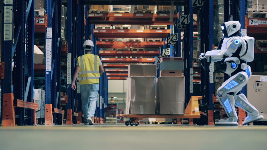 Worker stops robot to place an extra box to his cart at modern warehouse Royalty-Free Stock Footage #1063507039