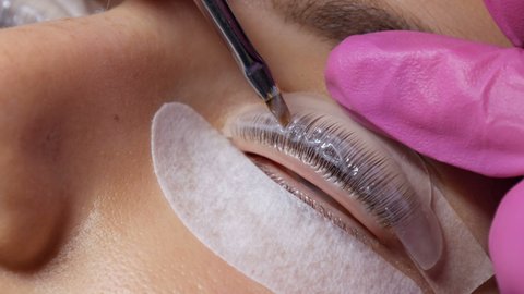 Face of a young girl before a modern eyelash lamination procedure in a professional beauty salon. The master applies a chemical during the eyelash curling procedure with a special brush close up.