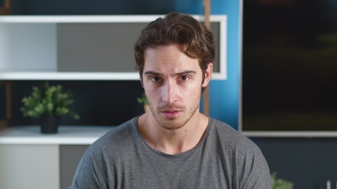 Shocked young man shows disgust at what he sees. Unpleasantly surprised male covers his mouth with his hand. Home or office apartment on background