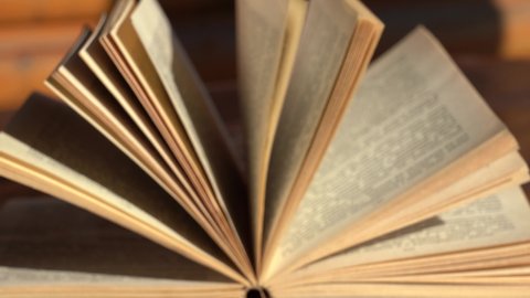 Closeup view 4k video of blurry unfocused old open paper book laying on wooden table on sunny terrace